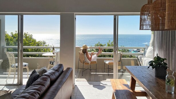 A modern living room with a large glass door leading to a balcony overlooking the sea. - Comfortable 3 Bedroom Apartment - Number 5103 (Cape Town)