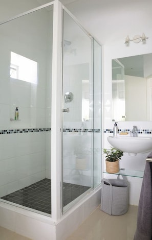 Ein modernes Badezimmer mit einer gläsernen Dusche, einem weißen Waschbecken und einem Spiegel.