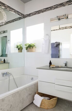 Ein modernes Badezimmer mit einer Badewanne, einem Waschtisch mit Spiegel und einer Topfpflanze.