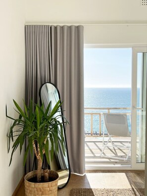 Enjoy the ocean view from this room's large window, featuring a balcony with a chair and a potted plant on the floor.