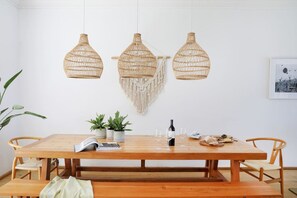 A wooden dining table with three hanging wicker pendant lights, potted plants, and a bottle of wine. - Beach House - Number 49 (Cape Town)