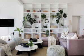 A modern living room with a sofa, a coffee table, and a bookshelf filled with books and plants. - Beach House - Number 49 (Cape Town)
