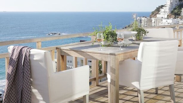 An outdoor dining area with a view of the sea, wooden flooring, and white chairs. - Beach House - Number 49 (Cape Town)