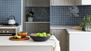 A modern kitchen with grey cabinets, a white countertop, and a blue-tiled backsplash. - Beach House - Number 49 (Cape Town)