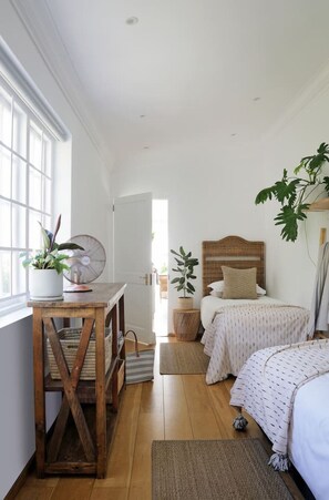 A bedroom with a wooden bed, a bedside table with a fan, and a window with a view. - Beach House - Number 49 (Cape Town)