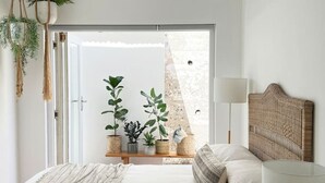A bedroom with a bed, bedside table, lamp, and potted plants. - Beach House - Number 49 (Cape Town)