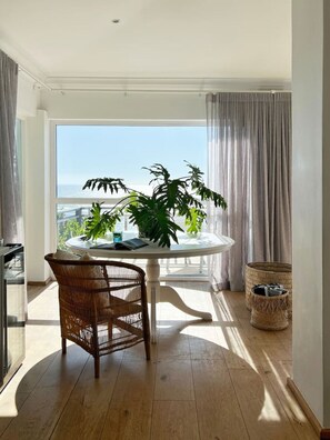 Enjoy a serene atmosphere with a clear sea view from this open-plan living area featuring a round table and wicker chair.