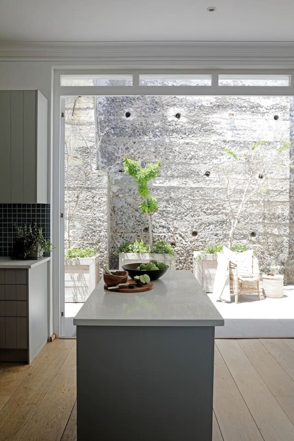 A modern kitchen with a central island, a stone wall, and a view of a garden.
