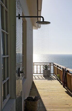 A wooden deck with a view of the ocean, a hanging shower, and a potted plant.