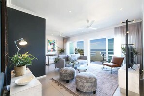 A modern living room with a sofa, ottomans, and a coffee table. There is a balcony with a view of the sky. - Contemporary Clifton Apartment - Number 5104 (Cape Town)