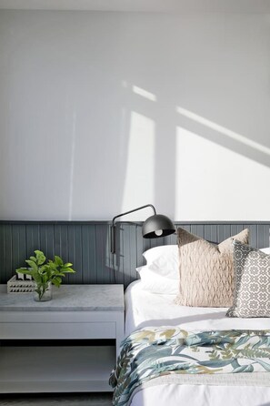 A bedroom with a bed, bedside table, lamp, and a potted plant. - Contemporary Clifton Apartment - Number 5104 (Cape Town)