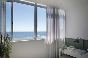 A bedroom with a large window overlooking the ocean, a bedside table with a lamp, and a potted plant. - Contemporary Clifton Apartment - Number 5104 (Cape Town)