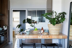 A kitchen with a wooden countertop, various plants, a wine bottle, and a dining area with chairs. - Contemporary Clifton Apartment - Number 5104 (Cape Town)