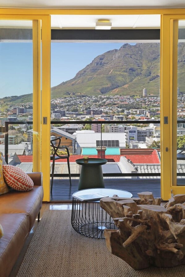 A modern living room with a sofa, a round table, and a view of a cityscape and mountain.