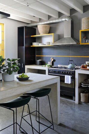 A modern kitchen with a central island, bar stools, a stove, and a large window.