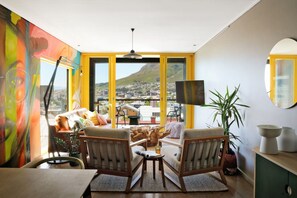 A room with a large window, a flat-screen TV, a sofa, and a dining table.