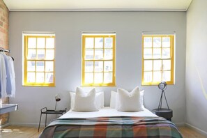 A bedroom with a bed, three windows, a desk, and a lamp.
