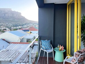 En balkon med udsigt over bybilledet, en stol, et lille bord og en gulrammet dør.