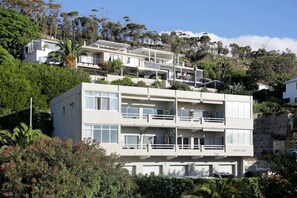 Un immeuble résidentiel à plusieurs étages, doté de balcons, situé sur une colline et entouré de verdure.