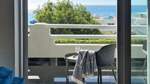 Un balcón con vista al mar, una silla, una mesita y un sofá azul.
