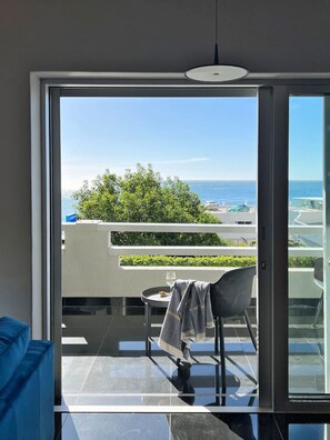 A balcony with a view of the sea, a chair, a small table, and a blue sofa. - Stylish Clifton Apartment - Number 5102 (Cape Town)