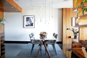 A modern dining area with a glass table, grey upholstered chairs, and a wooden accent wall. - Stylish Clifton Apartment - Number 5102 (Cape Town)
