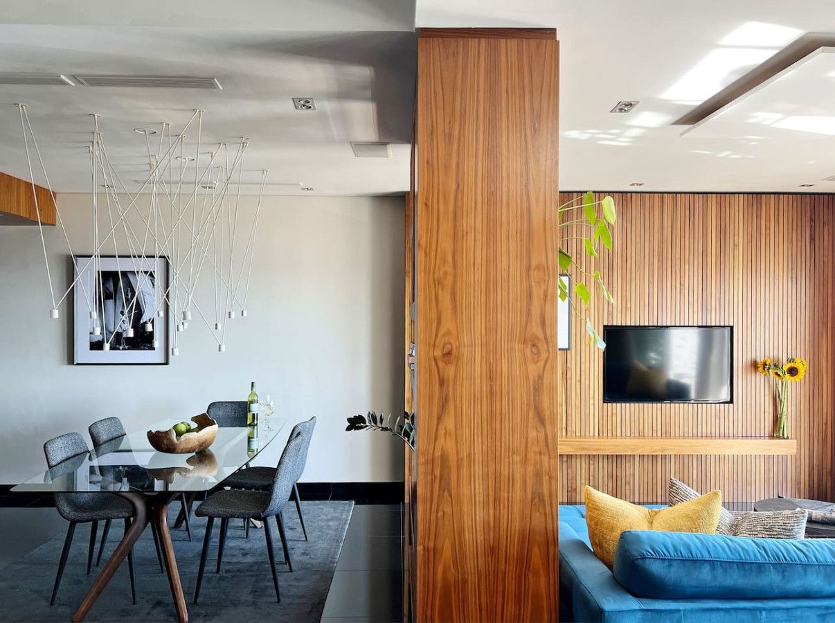 Un espace de vie moderne comprenant un coin repas, un téléviseur fixé à un mur en bois et un canapé bleu.