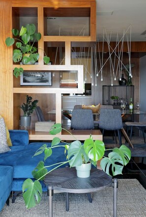 A modern living room with a blue sofa, a dining area with chairs, and a kitchen in the background. - Stylish Clifton Apartment - Number 5102 (Cape Town)