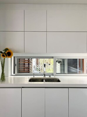 Une cuisine moderne dotée d’un évier encastré, de meubles blancs et d’une fenêtre avec des stores.