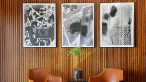 Una habitación con paneles de madera, dos sillas marrones y tres cuadros abstractos blanco y negro en la pared.