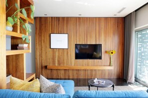A modern living room with a large flat-screen TV mounted on a wooden wall, a blue sofa, a small round coffee table, and a potted plant. - Stylish Clifton Apartment - Number 5102 (Cape Town)