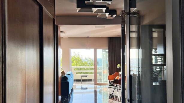 Un interior moderno con un ventanal de vidrio que da a un balcón, un sofá azul y un comedor.
