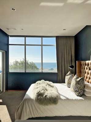 Une chambre avec une grande fenêtre, un lit avec une literie blanche et une vue sur la mer.