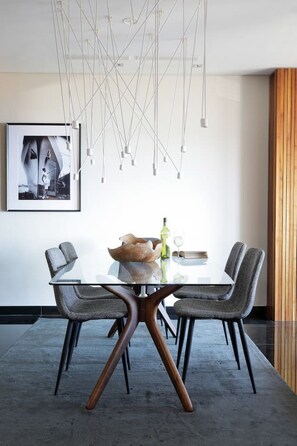 Un espace repas moderne avec une table en verre, des chaises à revêtement gris et un plancher en bois.