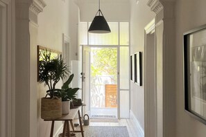 A hallway with a door leading to a balcony, a hanging light fixture, and framed pictures on the walls.