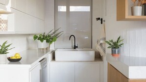 Une cuisine moderne avec des meubles blancs, un îlot central doté d’un évier et des plantes en pot.