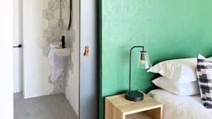 Une pièce avec un mur vert, une table de chevet en bois, un lit avec une literie blanche et un porte-serviettes suspendu.