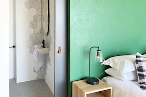 A room with a green wall, a wooden nightstand, a bed with white bedding, and a hanging towel rack. - Oldfield House - Number 29 (Cape Town)