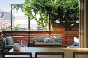 An outdoor seating area with a wooden bench, a sofa, and a table with wine glasses and bowls.