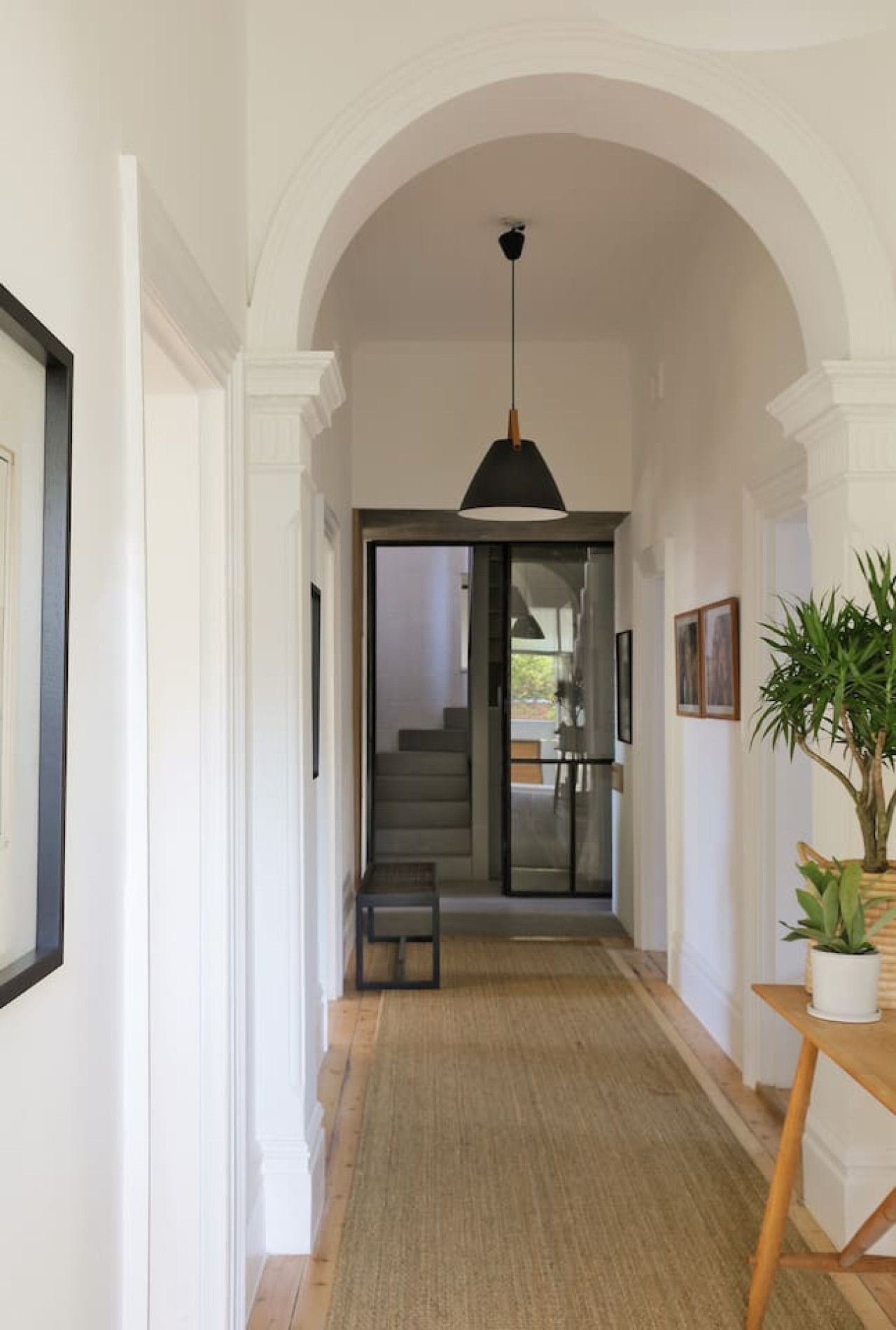 A hallway with an arched ceiling, a bench, a hanging light fixture, and a potted plant.