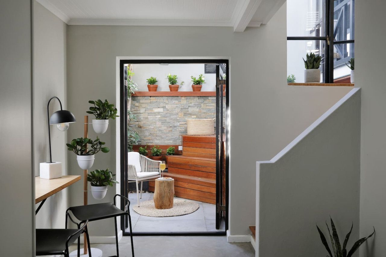 A modern interior with a staircase leading to a balcony, a dining area with a table and chairs, and potted plants.