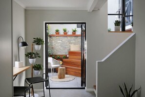A modern interior with a staircase leading to a balcony, a dining area with a table and chairs, and potted plants.