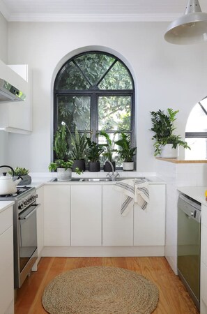 A modern kitchen with white cabinetry, a large arched window, and potted plants.