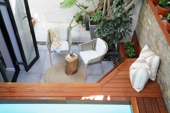 A wooden deck with two white chairs and a round wooden table, surrounded by potted plants and a stone wall.