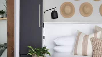 A bedroom with a bed, a bedside table with a plant, a wall-mounted lamp, and a door.