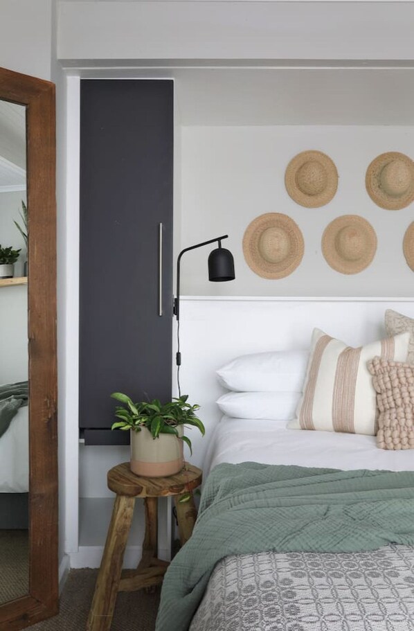 A bedroom with a bed, a bedside table with a plant, a wall-mounted lamp, and a door.