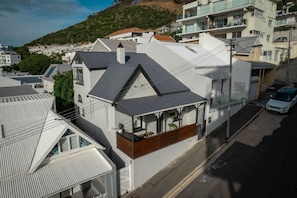 A residential building with a sloped roof, a balcony with wooden flooring, and a street view with a parked car.