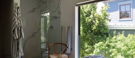 A bedroom with a large window, a shower, and a view of greenery outside.