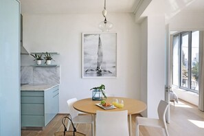 A dining area with a round table, chairs, a painting, and a view through a glass door.