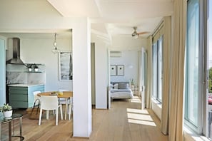 A modern kitchen with a dining area, a bedroom with a large window, and a hallway leading to a balcony.